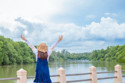 Rear view of woman standing by lake against sky