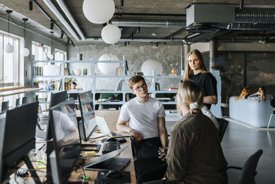Computer programmers talking to female colleague sitting in tech startup office