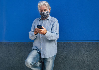 Man holding mobile phone while standing against wall
