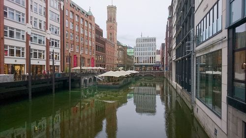 Canal by buildings in city against sky