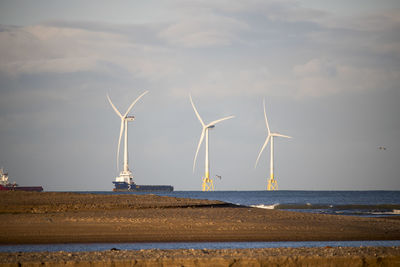 Wind turbines on beach against sky