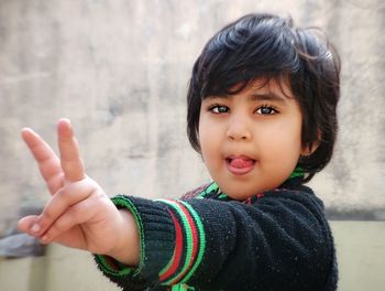 Portrait of cute girl gesturing peace sign against wall