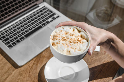 Close-up of hand holding coffee cup on table