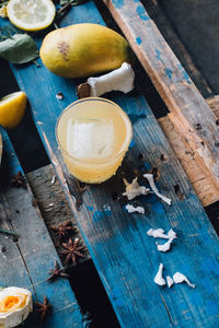 Yellow casual cocktail with ice, coconut, mango, star anise against blue wood pallet backdrop 