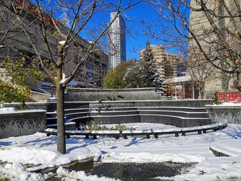Snow covered park by buildings against sky