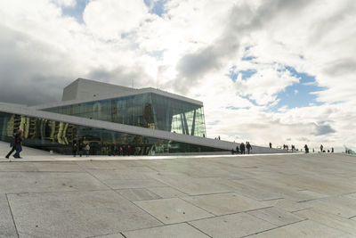 Low angle view of tourists at airport against cloudy sky