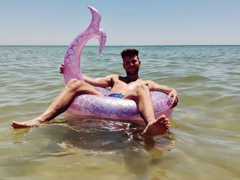 Portrait of shirtless man relaxing on inflatable ring in sea against sky