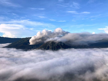 High angle view of sea of clouds surrounding bromo volcano erupting next to mount batok against sky