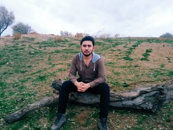 Portrait of smiling young man sitting on field against sky