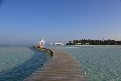 Pier over sea against clear blue sky
