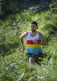 Sportsman looking away while running between grass on mountain at forest
