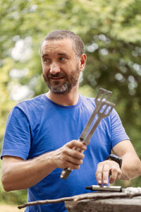 Smiling man holding serving tongs while standing in backyard