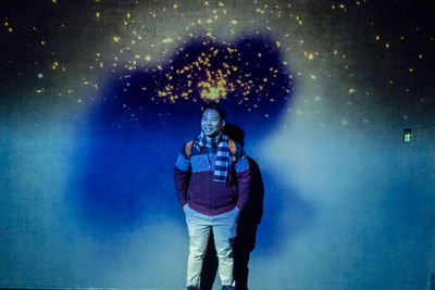 Full length portrait of a young man standing against star field at night