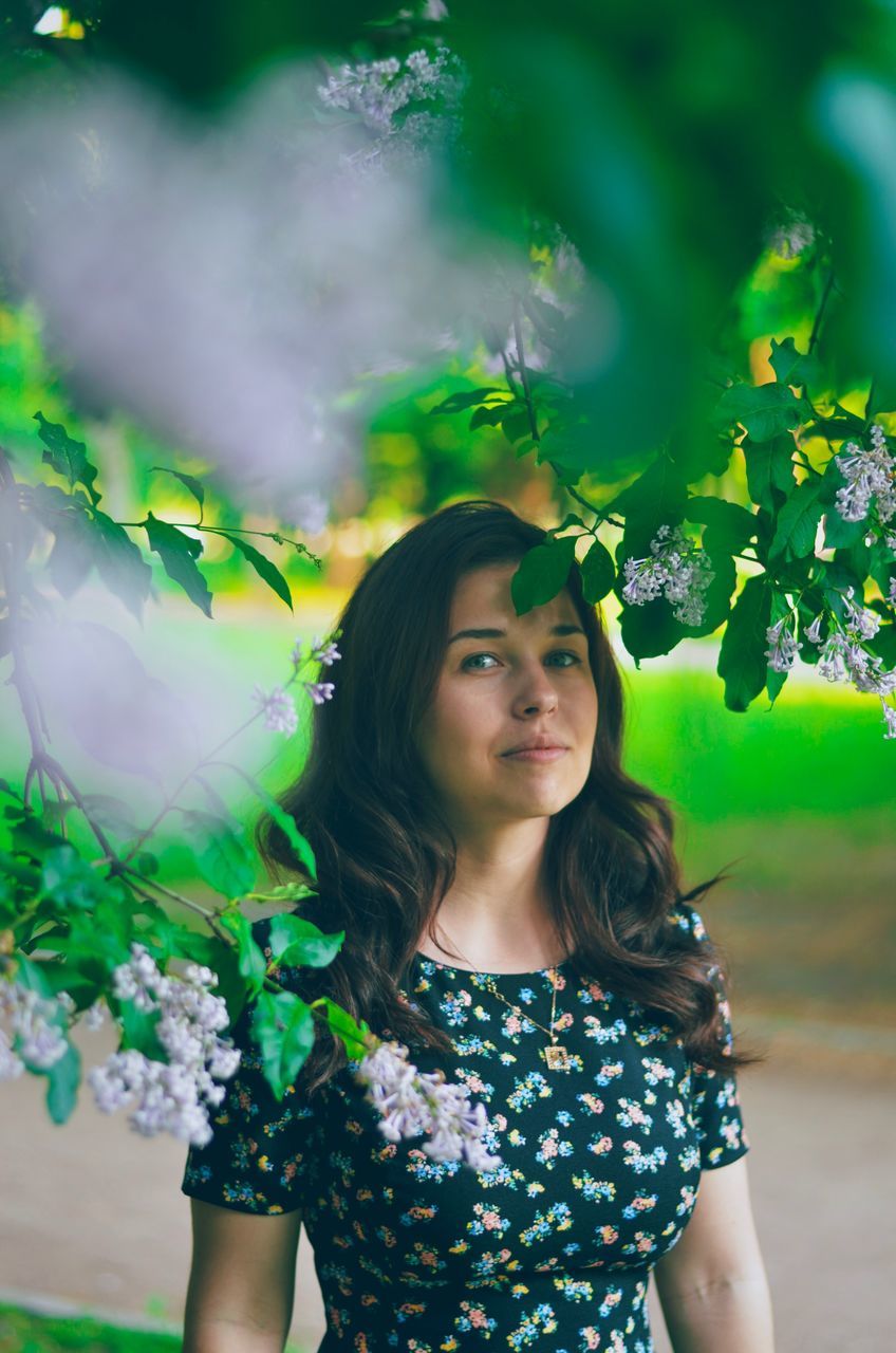 real people, leisure activity, one person, portrait, plant, lifestyles, nature, women, young women, looking at camera, beautiful woman, young adult, long hair, beauty, front view, casual clothing, flowering plant, leaf, standing, hairstyle, hair, outdoors