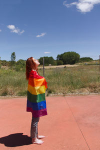 Side view full length of young woman with rainbow flag standing on sunny day