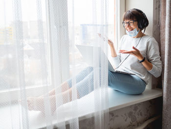 Businesswoman doing video call sitting on window sill at home