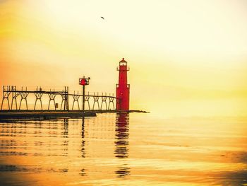 Lighthouse by sea against sky during sunset