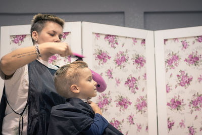 Barber blow drying hair of boy sitting on chair at shop