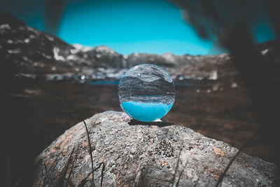 Close-up of crystal ball on rock against blue sky