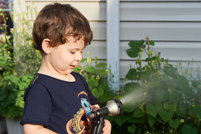 Little boy playing with a watering hose in the backyard