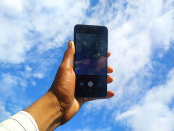 Low angle view of hand using mobile phone against sky