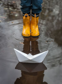 Boy standing in front of paper boat in puddle