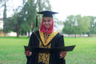 Portrait of smiling woman in graduation gown on field