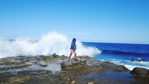 Rear view of woman standing on sea shore against clear sky