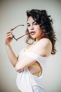 Portrait of beautiful young woman holding eyeglasses while standing against white background