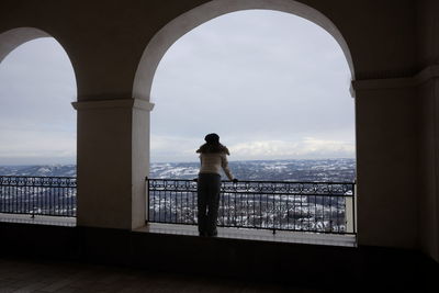 Rear view of woman looking at cloudy sky while standing in old building