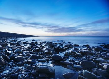 Pebbles on shore against cloudy sky during sunset