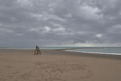 Rear view of woman walking at beach against cloudy sky