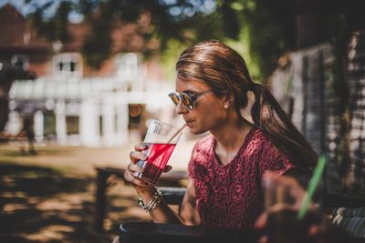 Young woman drinking glass while sitting outdoors