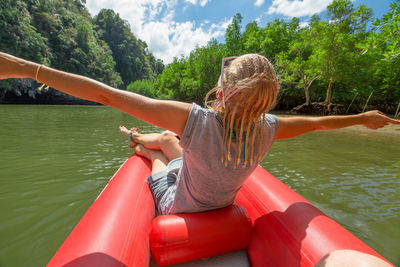 Woman sitting on inflatable raft over lake against trees