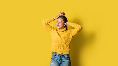 Young woman standing against yellow background