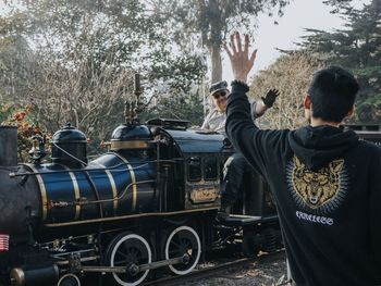 Rear view of man standing on street against trees