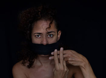 Portrait of young woman covering face against black background