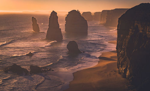 Rock formation on beach against sky during sunset