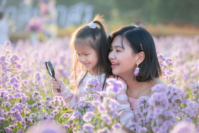 Close-up of daughter holding magnifying glass over purple flowering plants by mother