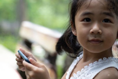 Portrait of cute girl holding smart phone outdoors