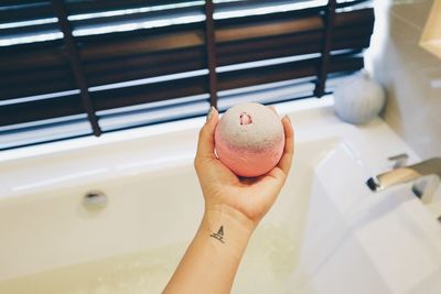 Cropped hand of woman holding object over bathtub at home