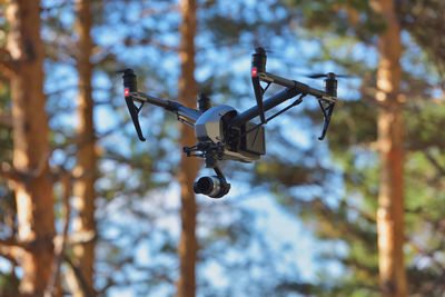 Low angle view of quadcopter flying against trees in forest