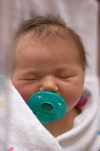 Close-up of newborn baby with green pacifier in hospital