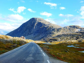 Country road by mountains against sky