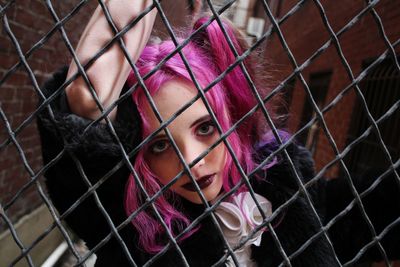 Portrait of young woman seen through chainlink fence