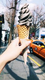 Cropped hand holding ice cream cone on street