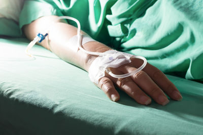 Midsection of woman with iv drip lying down on bed at hospital