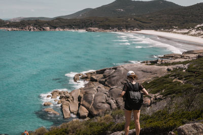 Rear view of woman standing on rock against sea