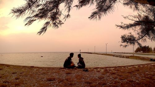 Side view of friends looking at sea against sky during sunset