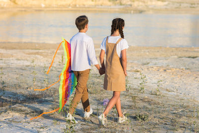 A girl and a boy holding hands go to launch a kite into the sky.